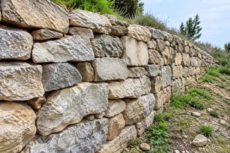 Mur de soutènement en blocs de pierre sèche stabilisant un terrain en pente sans béton.
