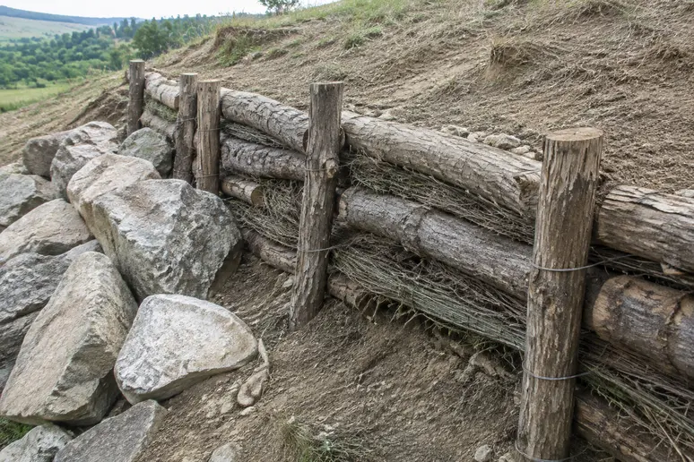 Fascine végétale en bois installée sur un talus sec aux côtés de blocs de pierre.