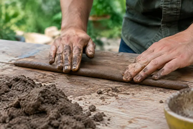 Mains de jardinier modelant une boule de terre argileuse compactée sur un établi en bois